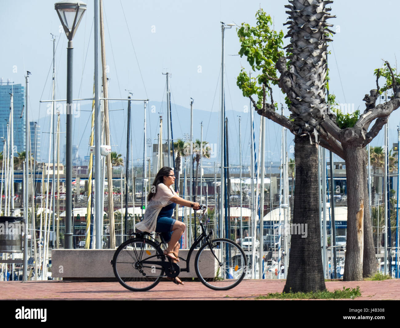 A young female adult riding a bicycle at the Olympic Port, Barcelona, Spain. Stock Photo