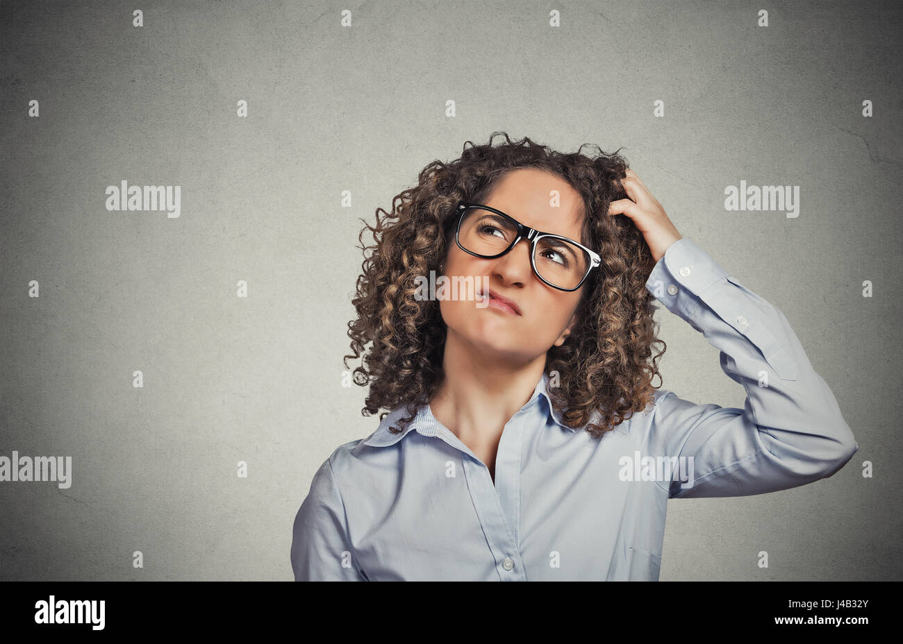 Closeup portrait young woman with glasses scratching head, thinking daydreaming something looking up isolated grey wall background. Human facial expre Stock Photo