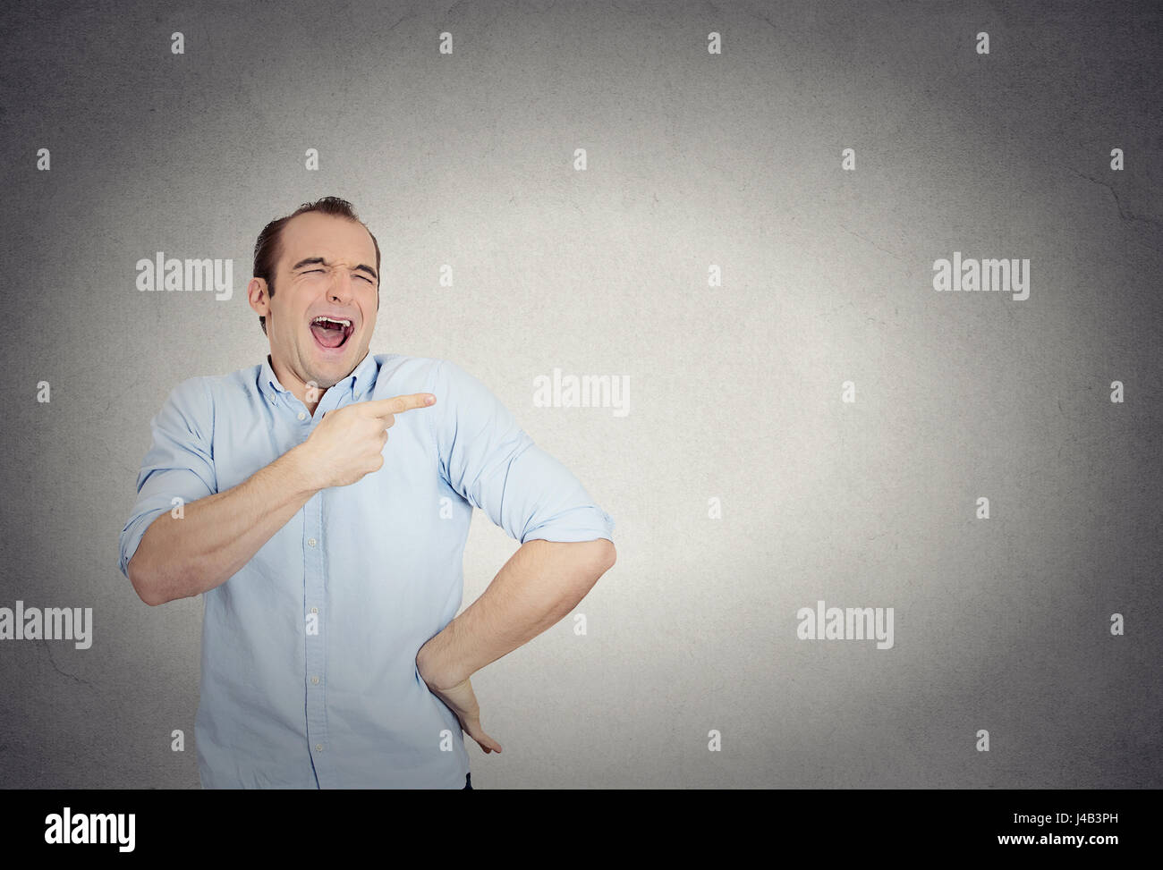 Closeup portrait of young man, laughing, pointing with finger, arms at someone, something, isolated grey wall background. Positive human face expressi Stock Photo