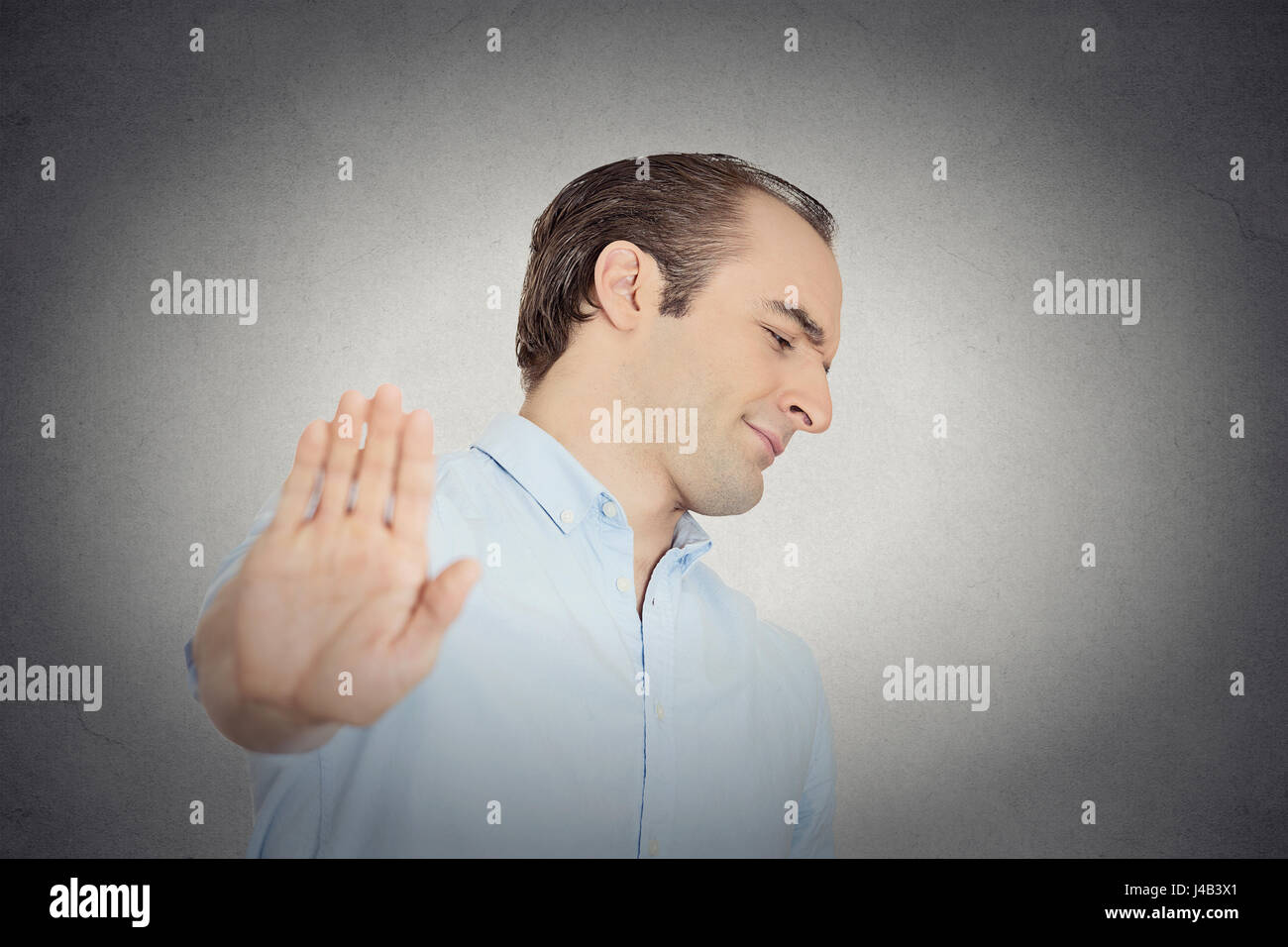 Closeup portrait young handsome grumpy man with bad attitude giving talk to hand gesture with palm outward isolated grey wall background. Negative emo Stock Photo