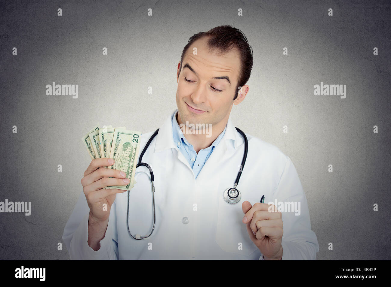 Closeup portrait grumpy greedy miserly health care professional, male doctor holding, protecting his money dollars in hand isolated grey wall backgrou Stock Photo
