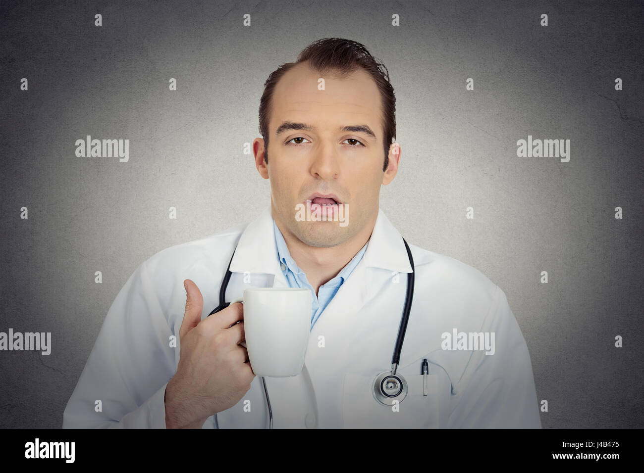 Portrait sleepy exhausted young funny doctor holding cup coffee tired busy day night shift trying to stay awake almost asleep isolated grey background Stock Photo