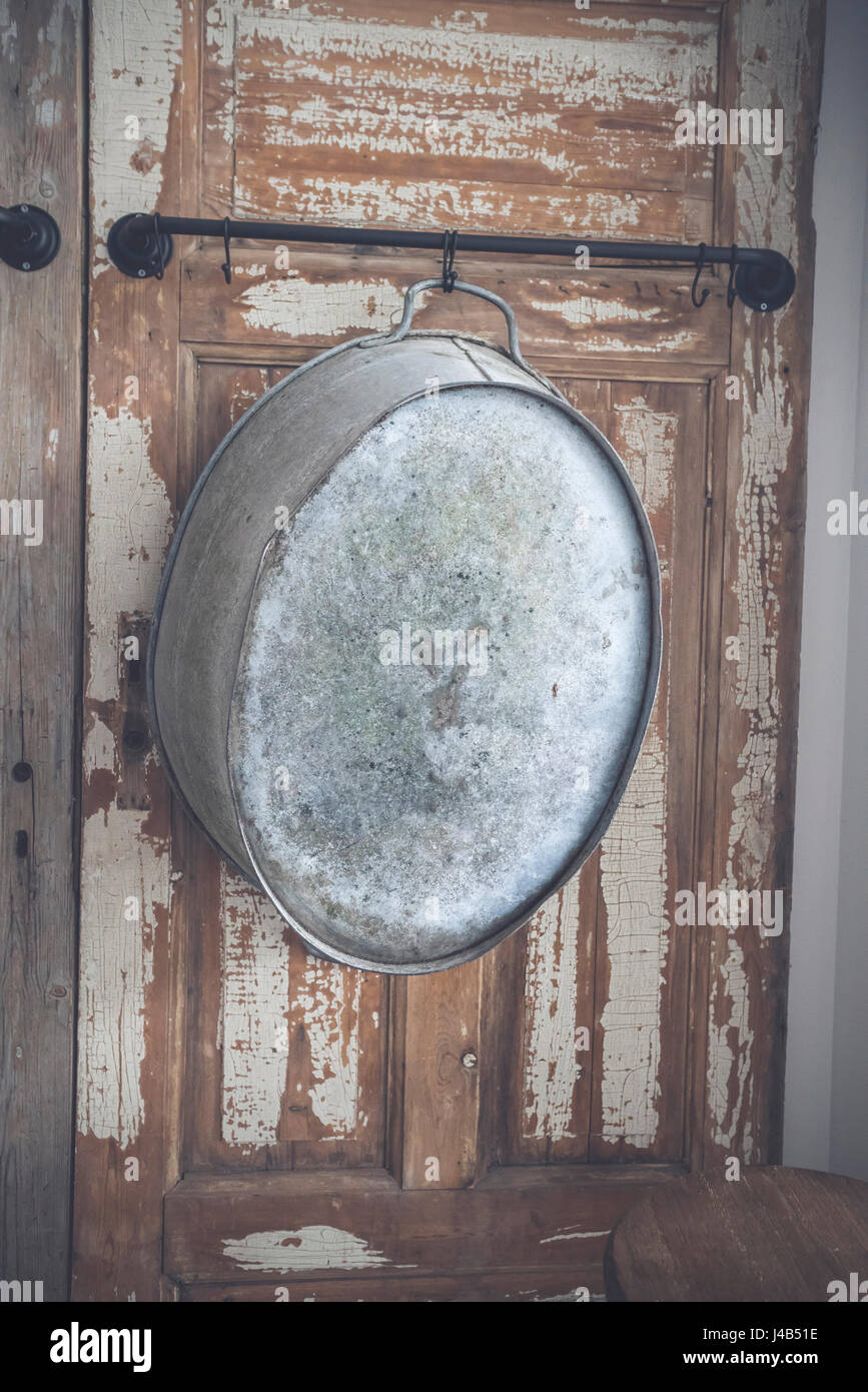 Old stylish iron tub hanging on a wooden wall with grunge paint peeling