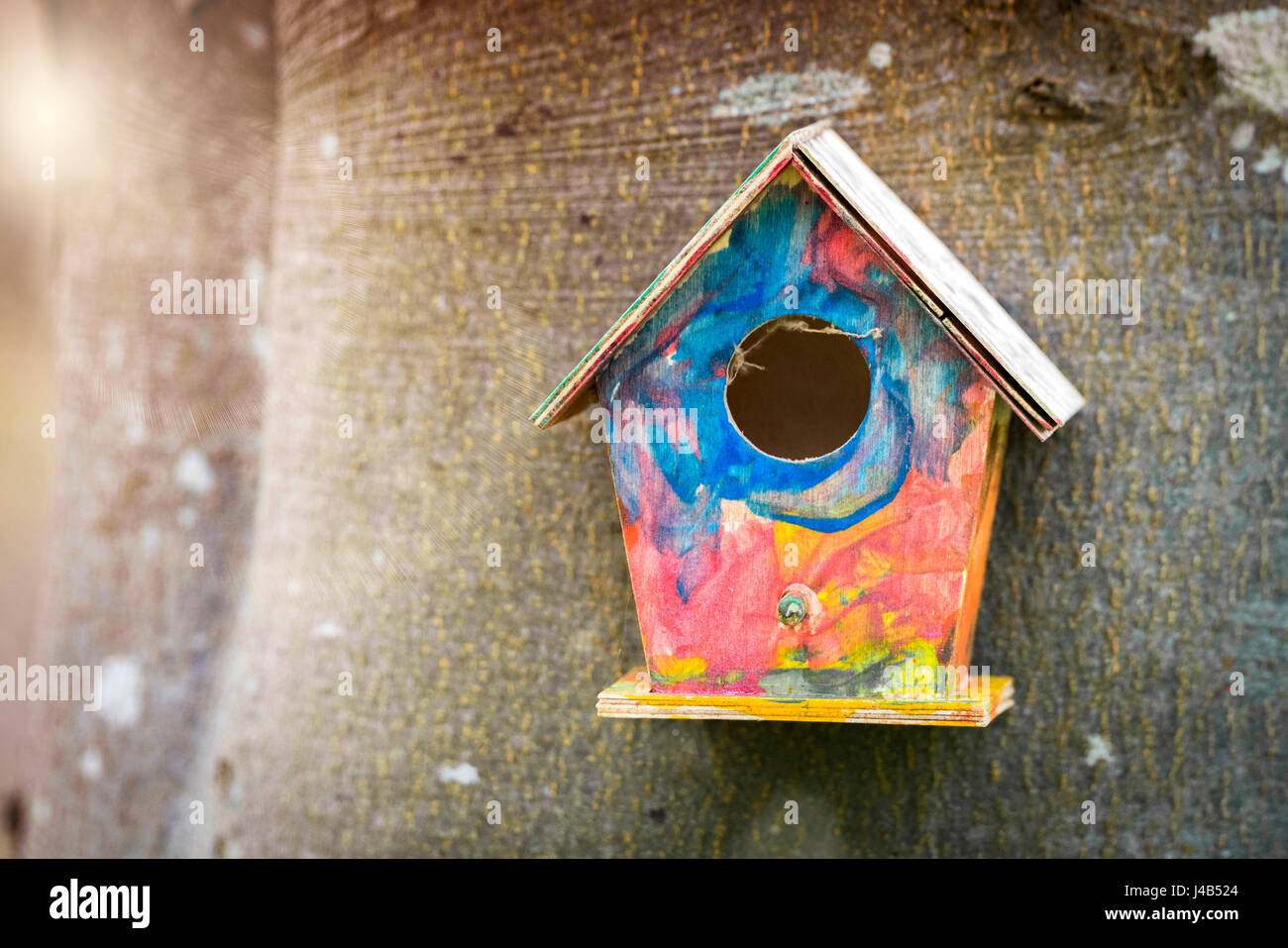 Colorful bird house in childish colors hanging on a tree in a garden in the spring Stock Photo