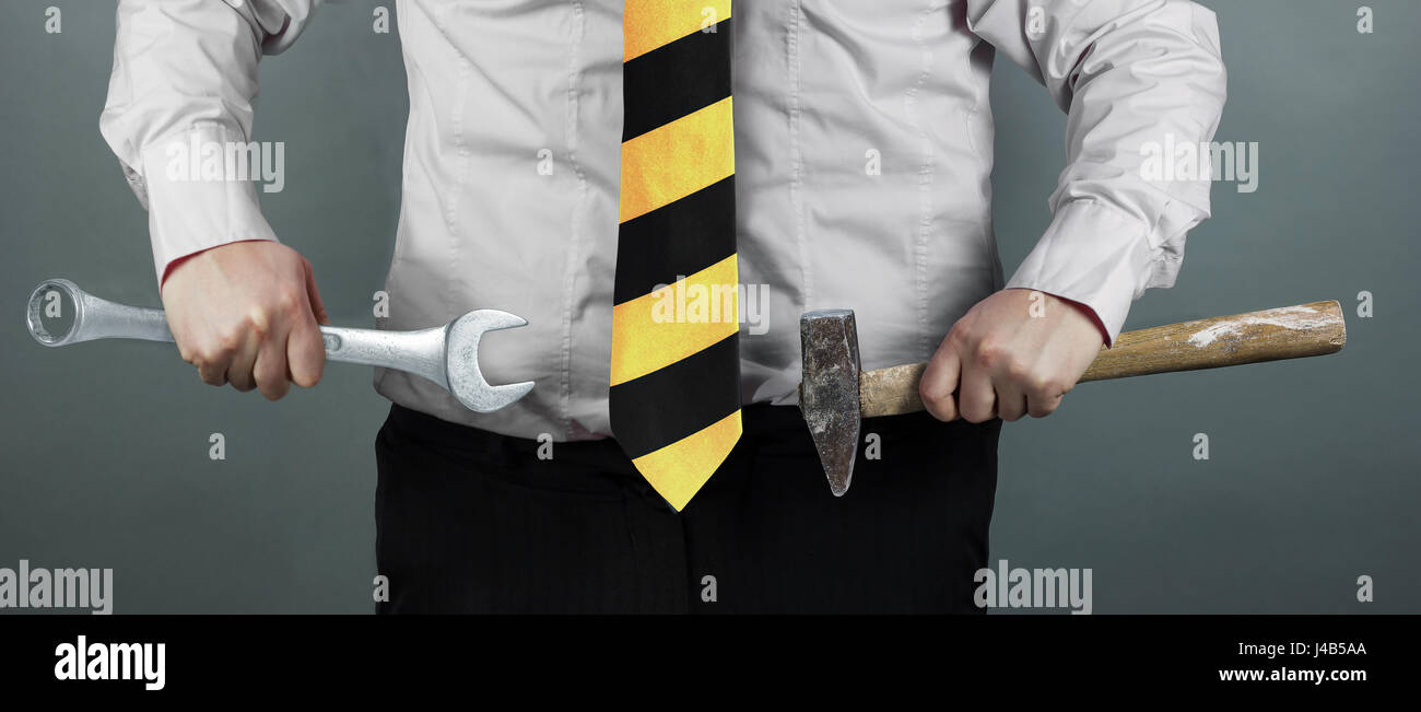 businessman holding hammer and spanner in hand and working zone black and yellow stripes cravat Stock Photo