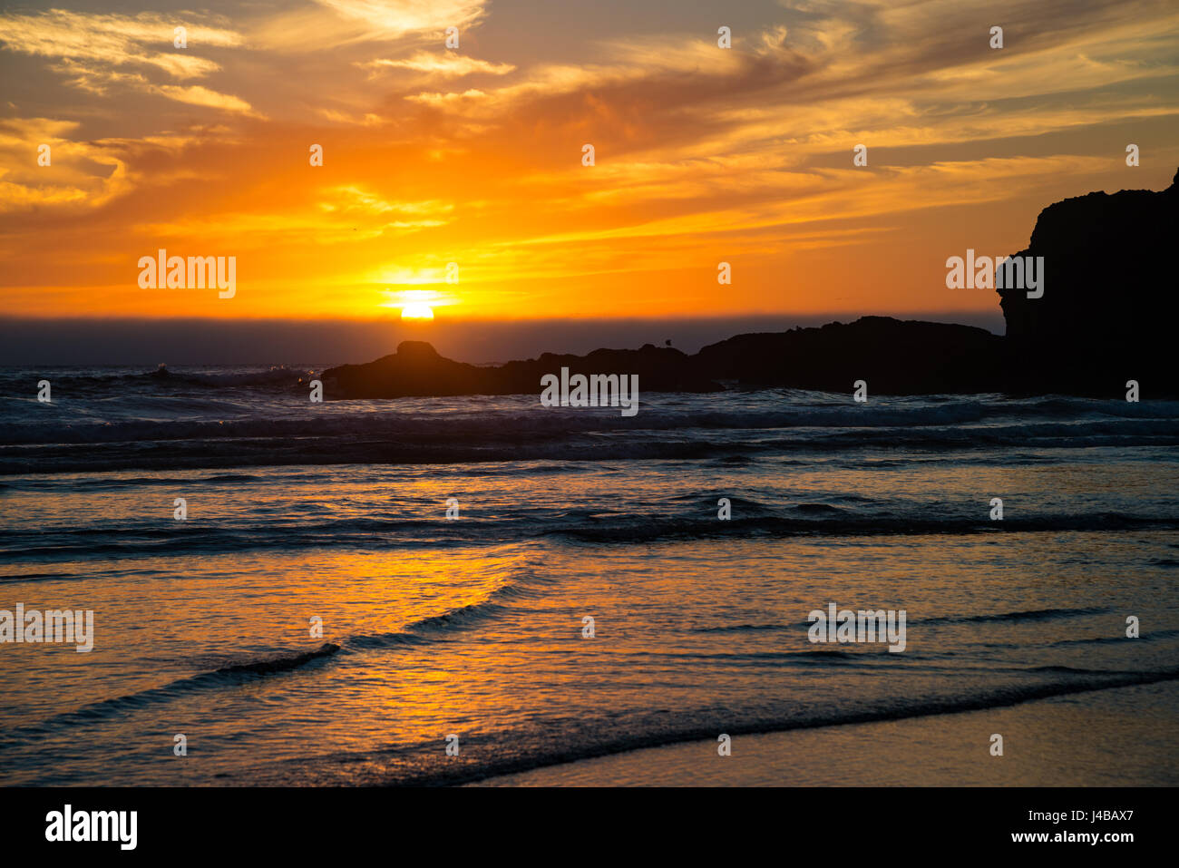 Orange sunset and waves on beach on Central Oregon coast Stock Photo