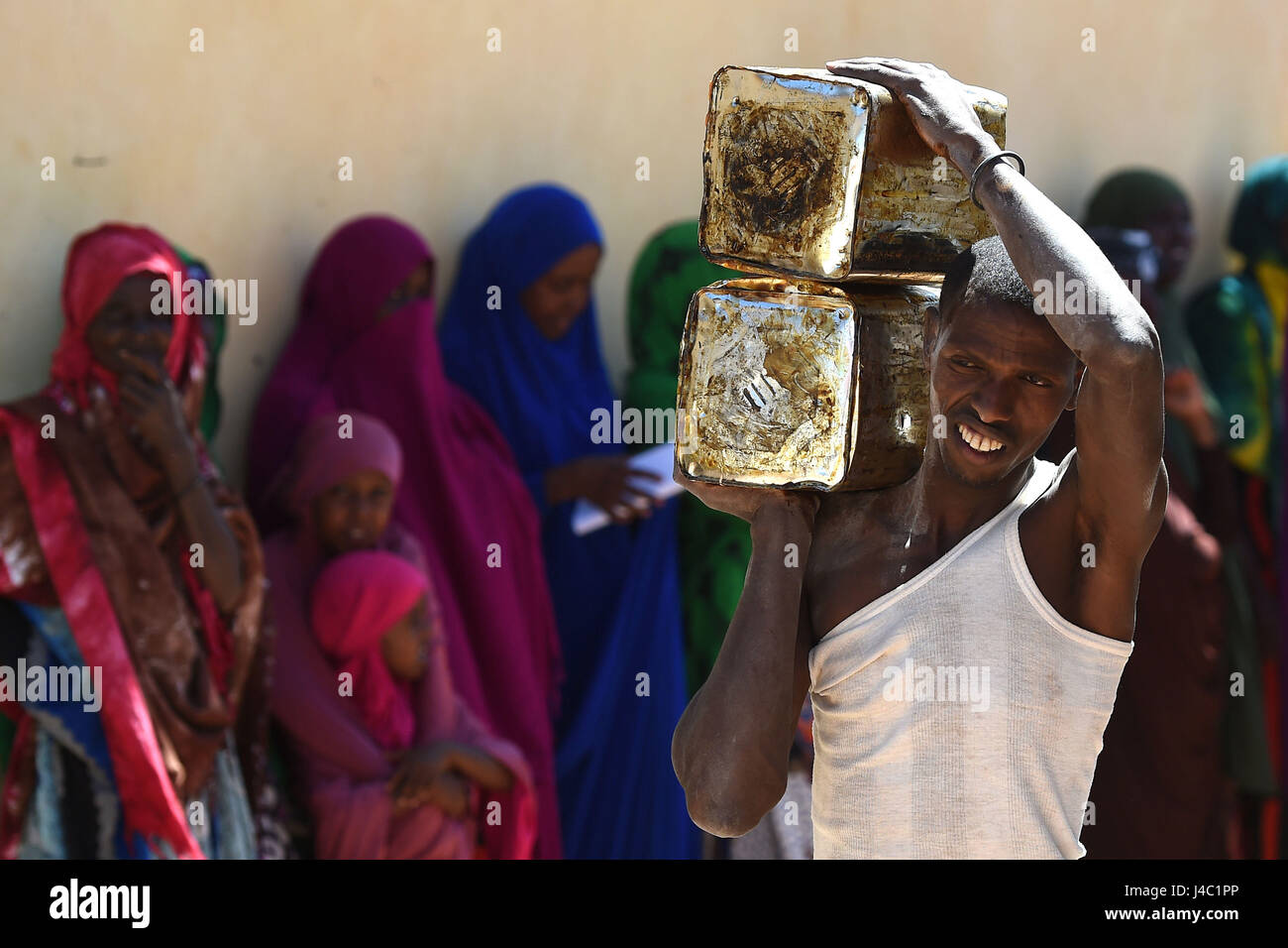 Villagers wait as tins of palm oil are delivered as part of the food distribution from charity Action Aid in Sayla Bari, Somaliland. Stock Photo