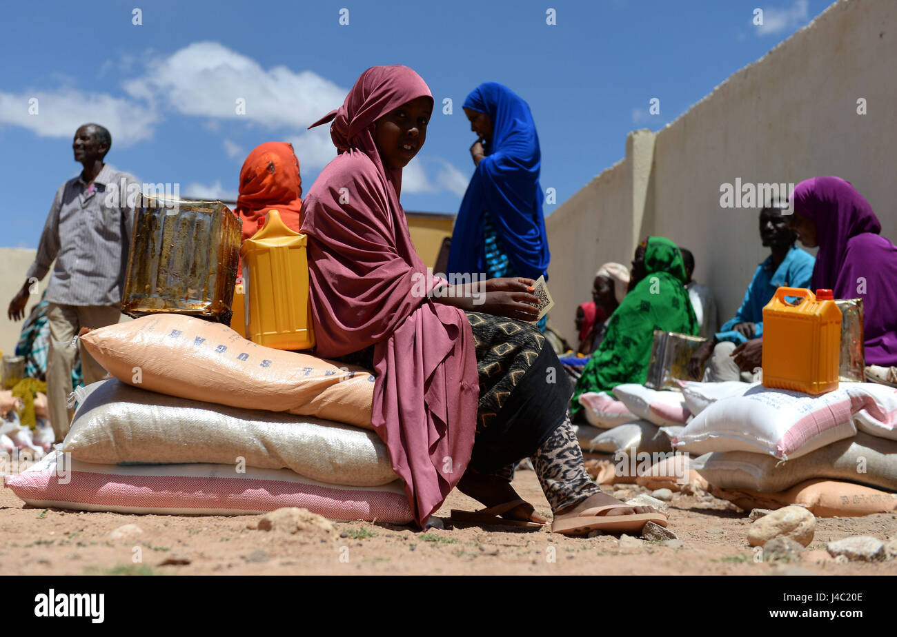 Villagers sit on their bags of rice, sugar, dates and palm oil during the food distribution from charity Action Aid in Sayla Bari, Somaliland. Stock Photo