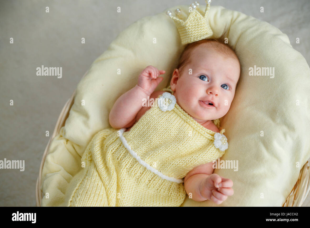 Portrait of newborn baby girl lying in a basket with golden crown and yellow bodysuit Stock Photo