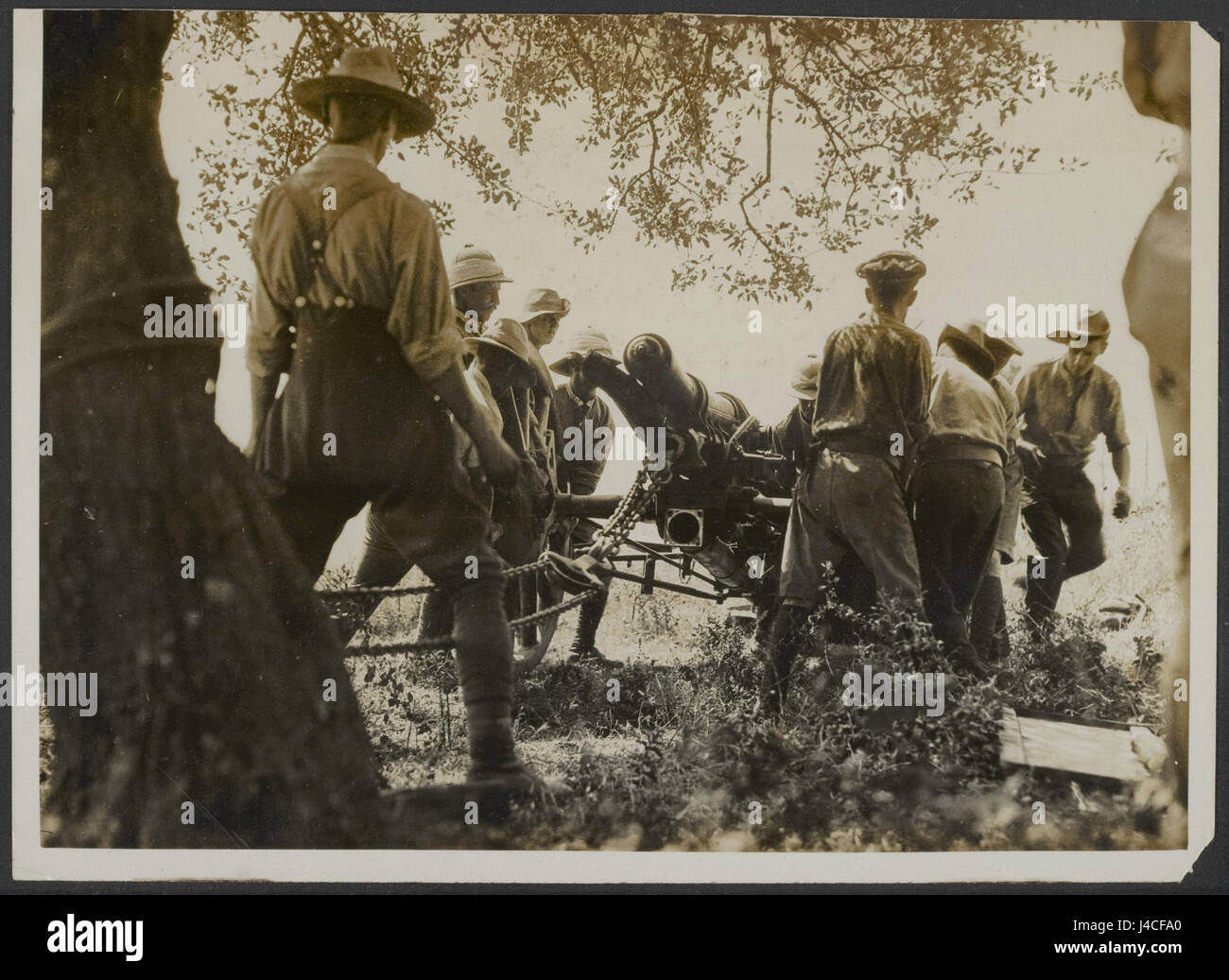 This photograph shows the process of repairing damage in a field workshop. Workers use brazing techniques on a broken piece of equipment, utilizing a tree as a support to pull out the damaged parts. The image is part of an archive of historical repair methods. Stock Photo