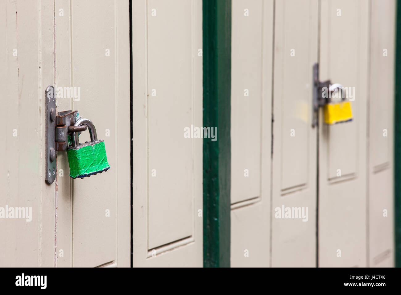 Coloured padlocks on a metal clasp, securing wooden doors. Stock Photo