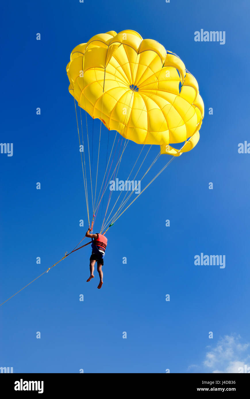 Skydiver on yellow parachute in sunny blue sky. Active lifestyle. Extreme sport. Stock Photo