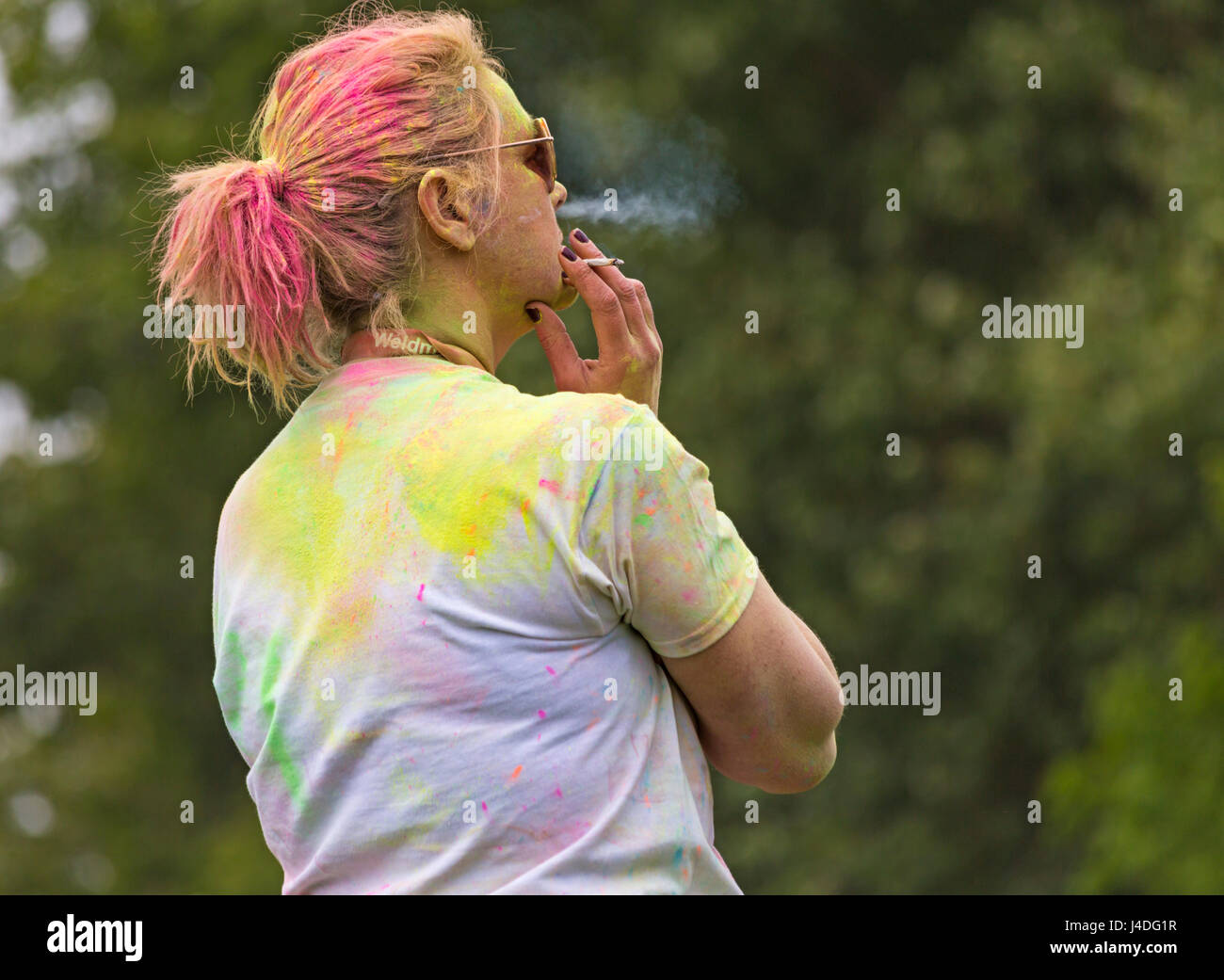 Woman smoking roll up cigarette covered in powder paint after Colour Run at Weymouth, Dorset in May Stock Photo