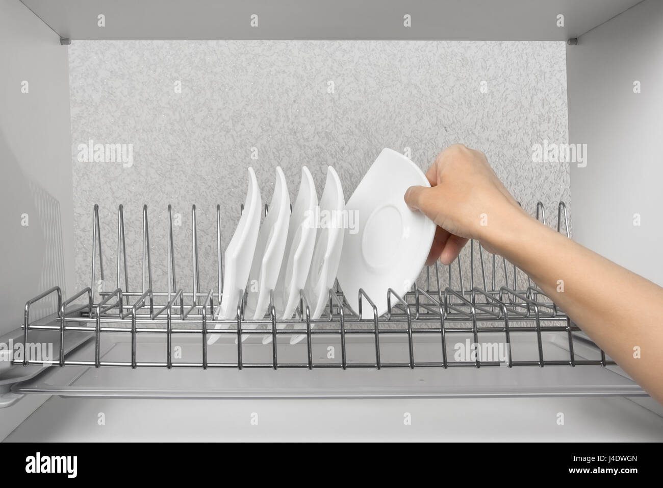 hand of woman putting just washed clean plate in the dish rack Stock Photo