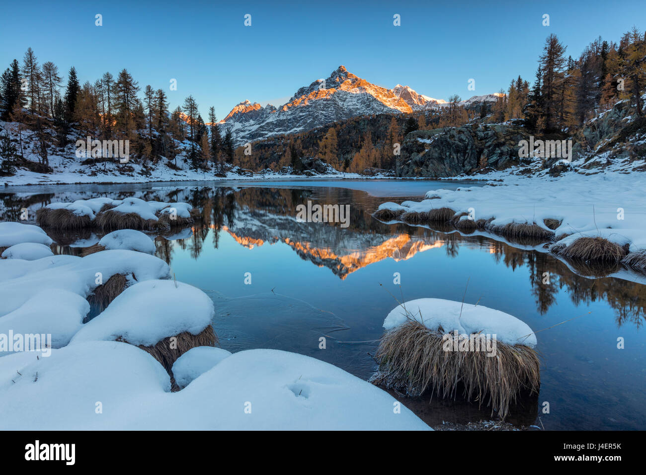 The rocky peak reflected in the frozen Lake Mufule at dawn, Malenco Valley, Province of Sondrio, Valtellina, Lombardy, Italy Stock Photo