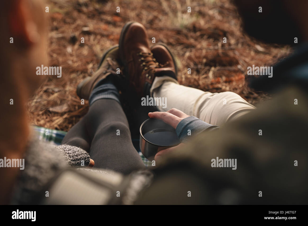 Close up of young couple sitting together outdoors, focus on hands holding cup of coffee. Hikers resting on mountain trail. Stock Photo