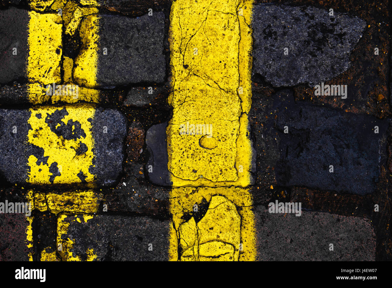 Double yellow lines with cracked paint on a cobbled London street. vertical composition, rule of thirds. Stock Photo