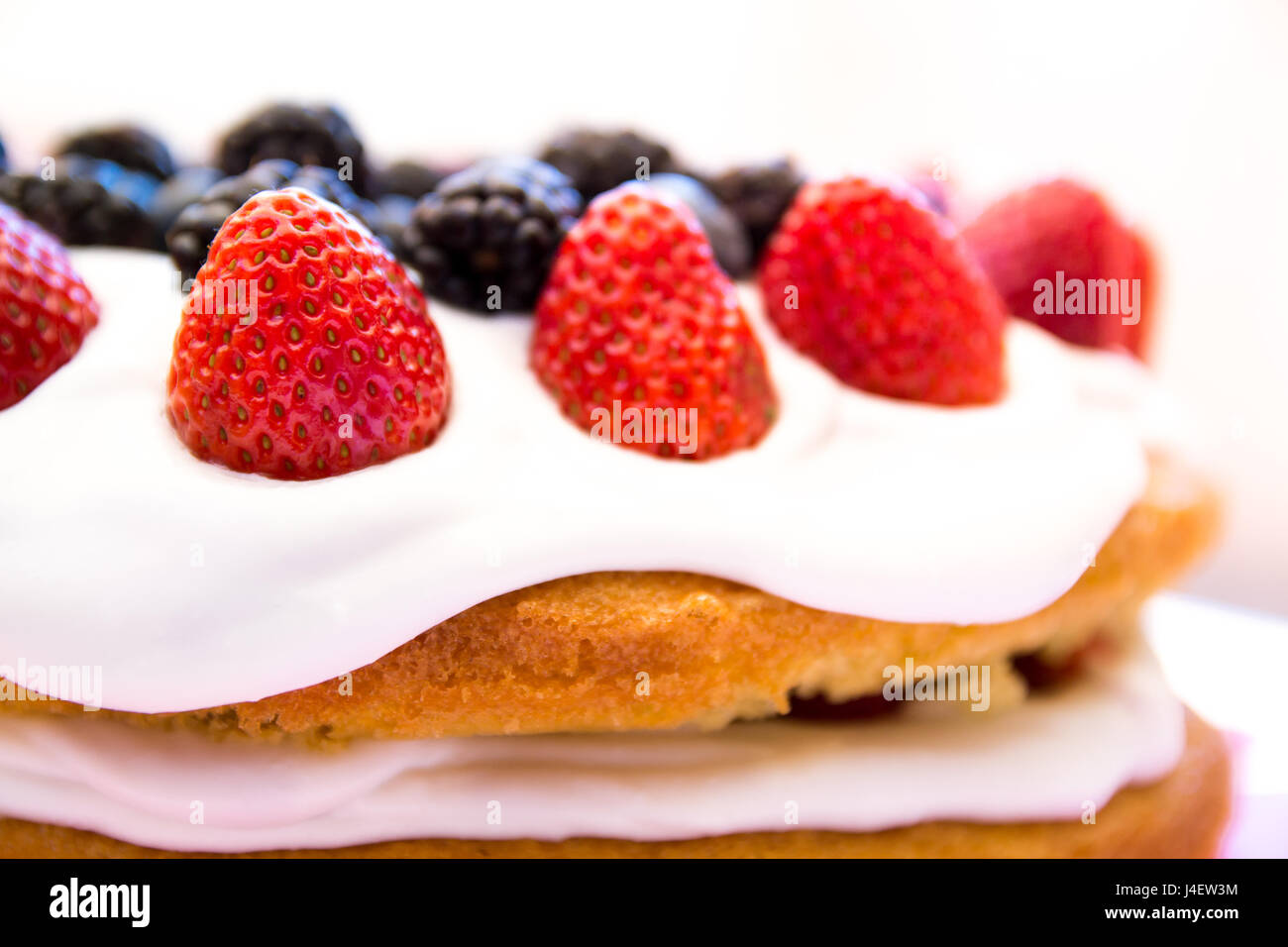 Light sponge cake with white icing and mixed berries (strawberries, blackberries, blueberries) on top. Bright light, warm perfect for summer. Stock Photo
