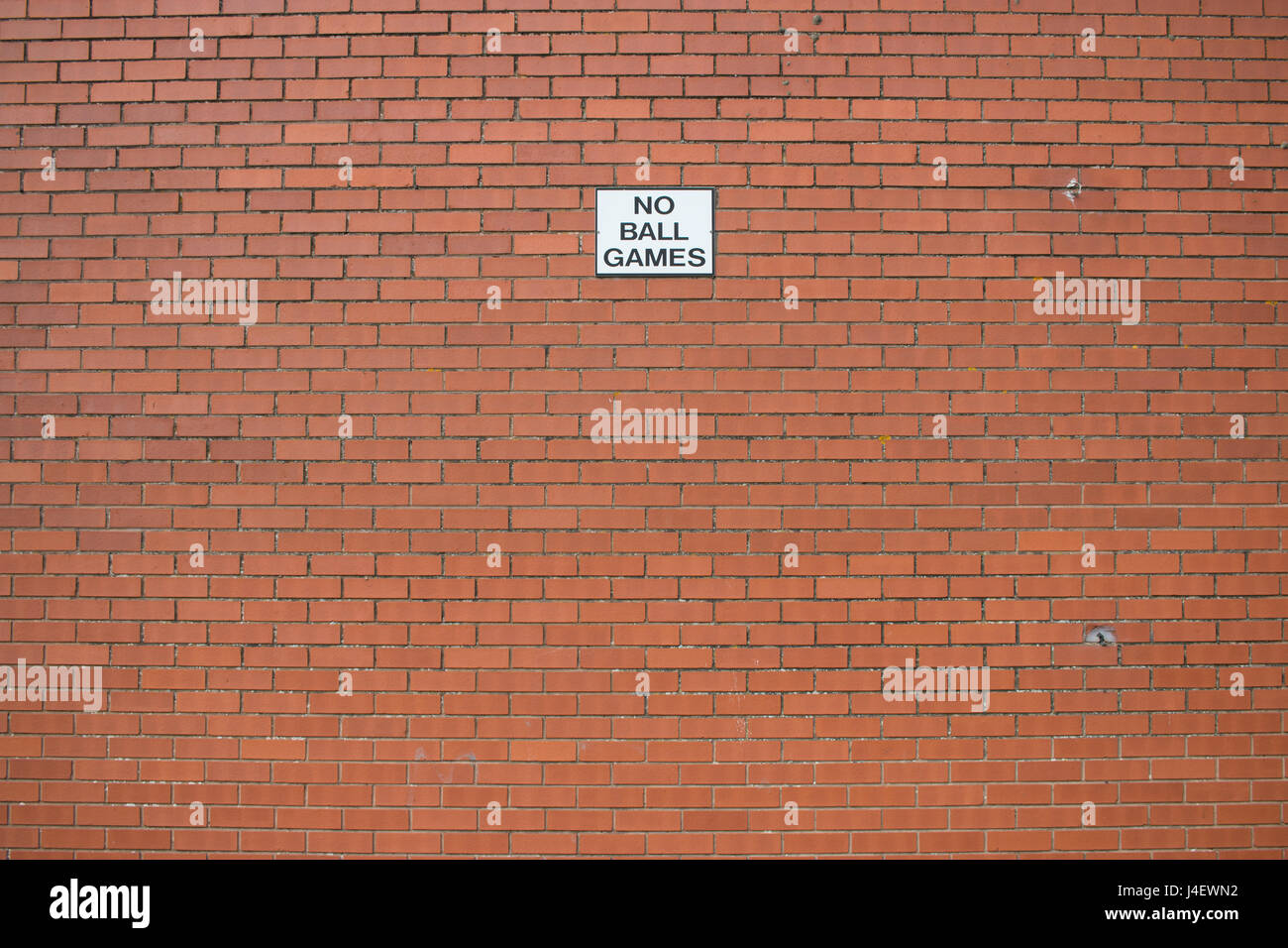 A large empty brick wall with a sign saying 'No Ball Games' Stock Photo