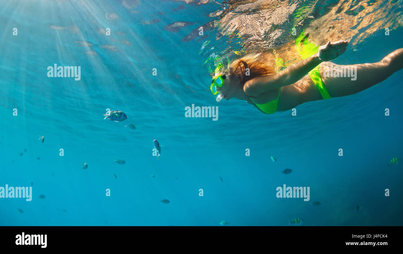 Happy family - girl in snorkeling mask dive underwater with fishes school in coral reef sea pool. Travel lifestyle, water sport outdoor adventure. Stock Photo