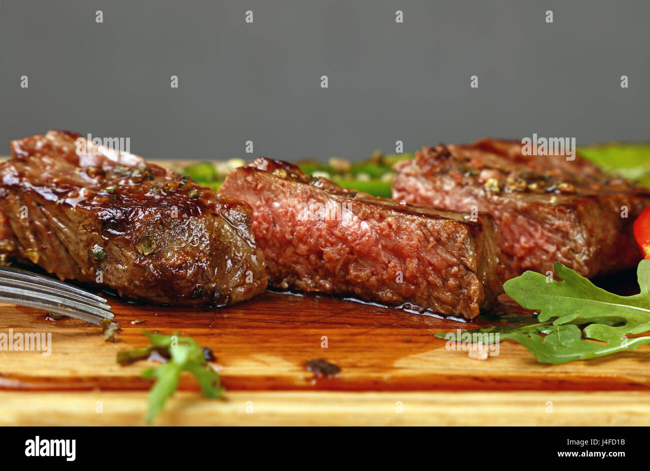 Cut slices of grilled juicy medium cooked beefsteak served on wooden board with fresh green rocket salad, close up, low angle view Stock Photo