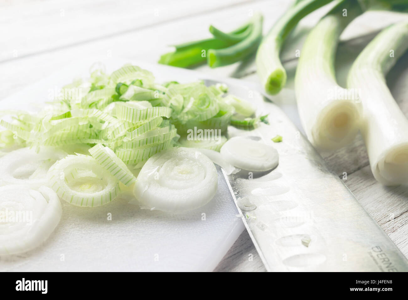Spring onions chopped on white board, with knife blade and some whole ...