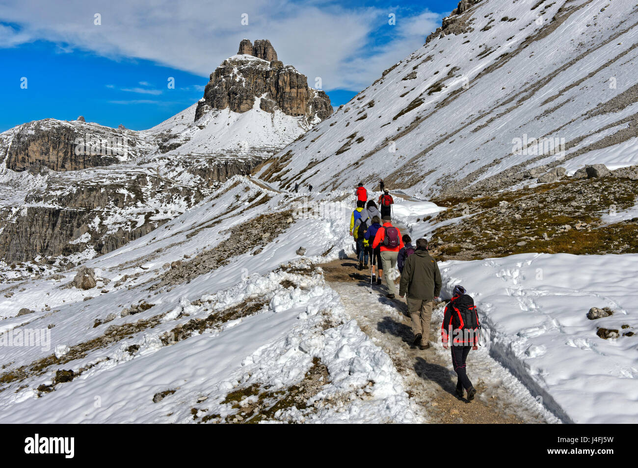 Hikers on the snow-covered hiking trail of the Three Peaks Circular Walk in front of the Tower of Toblin, Torre di Toblin, Sesto Dolomites, Italy Stock Photo