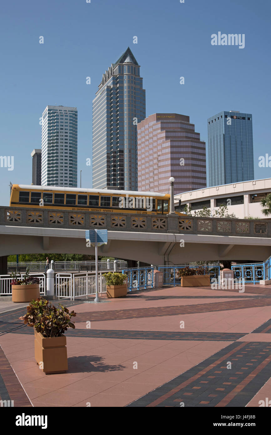 The highrise buildings of downtown Tampa Florida USA and the Tampa Riverwalk with a yellow school bus passing over. May 2017. Stock Photo