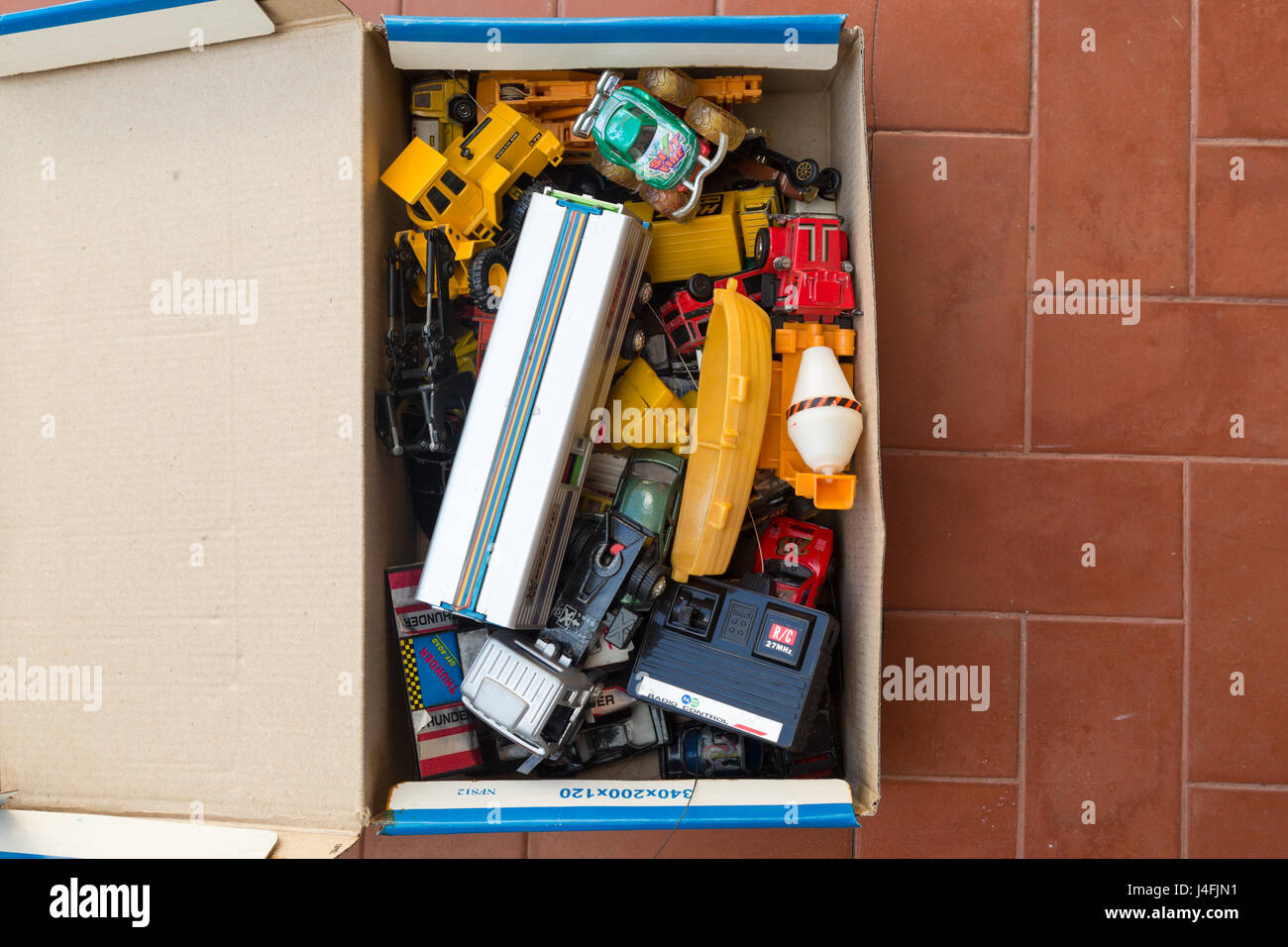 A box of old toys on red tile floor, flat lay Stock Photo