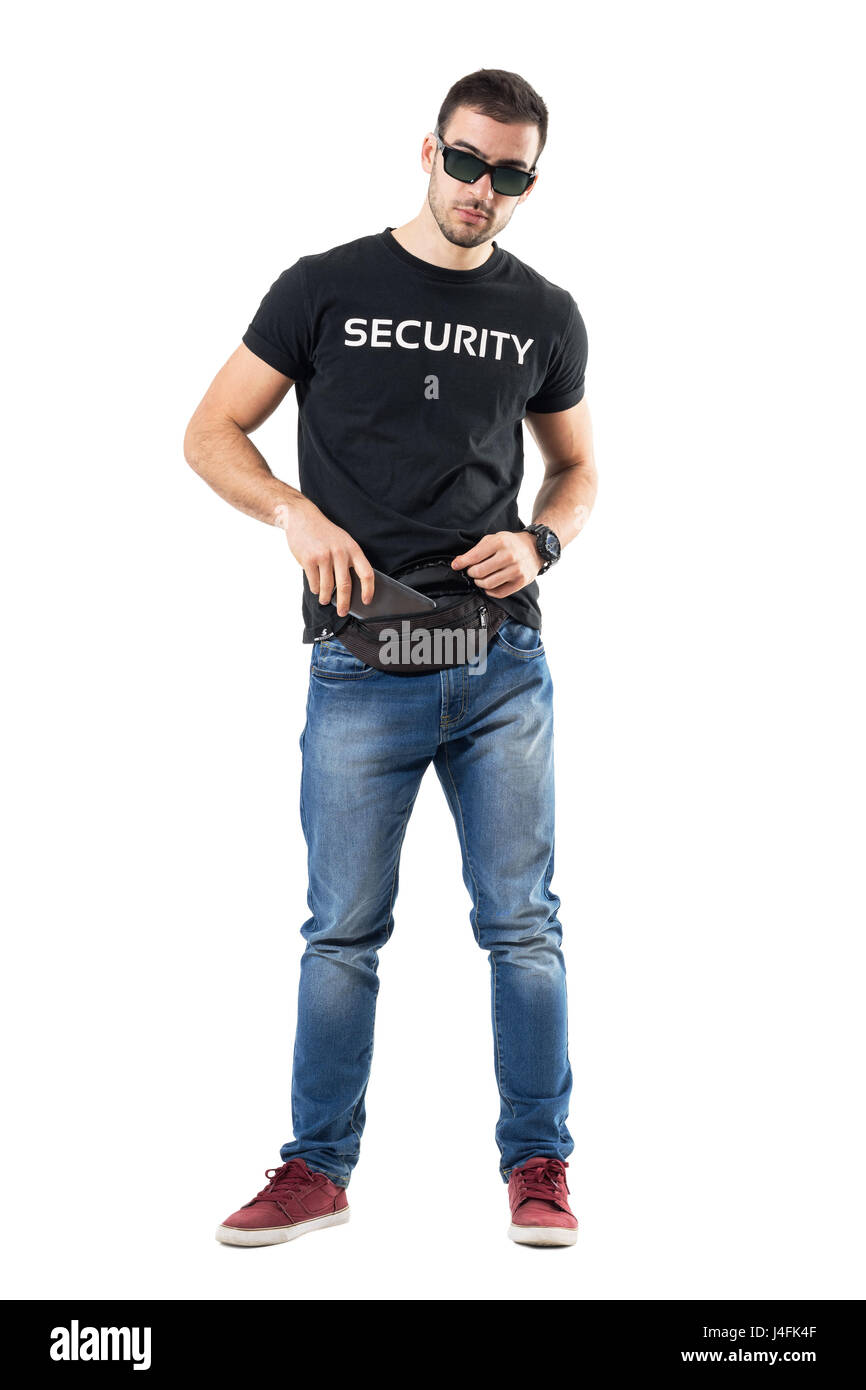 Undercover policeman in plain clothes put mobile phone in waist bag. Full body length portrait isolated on white studio background. Stock Photo