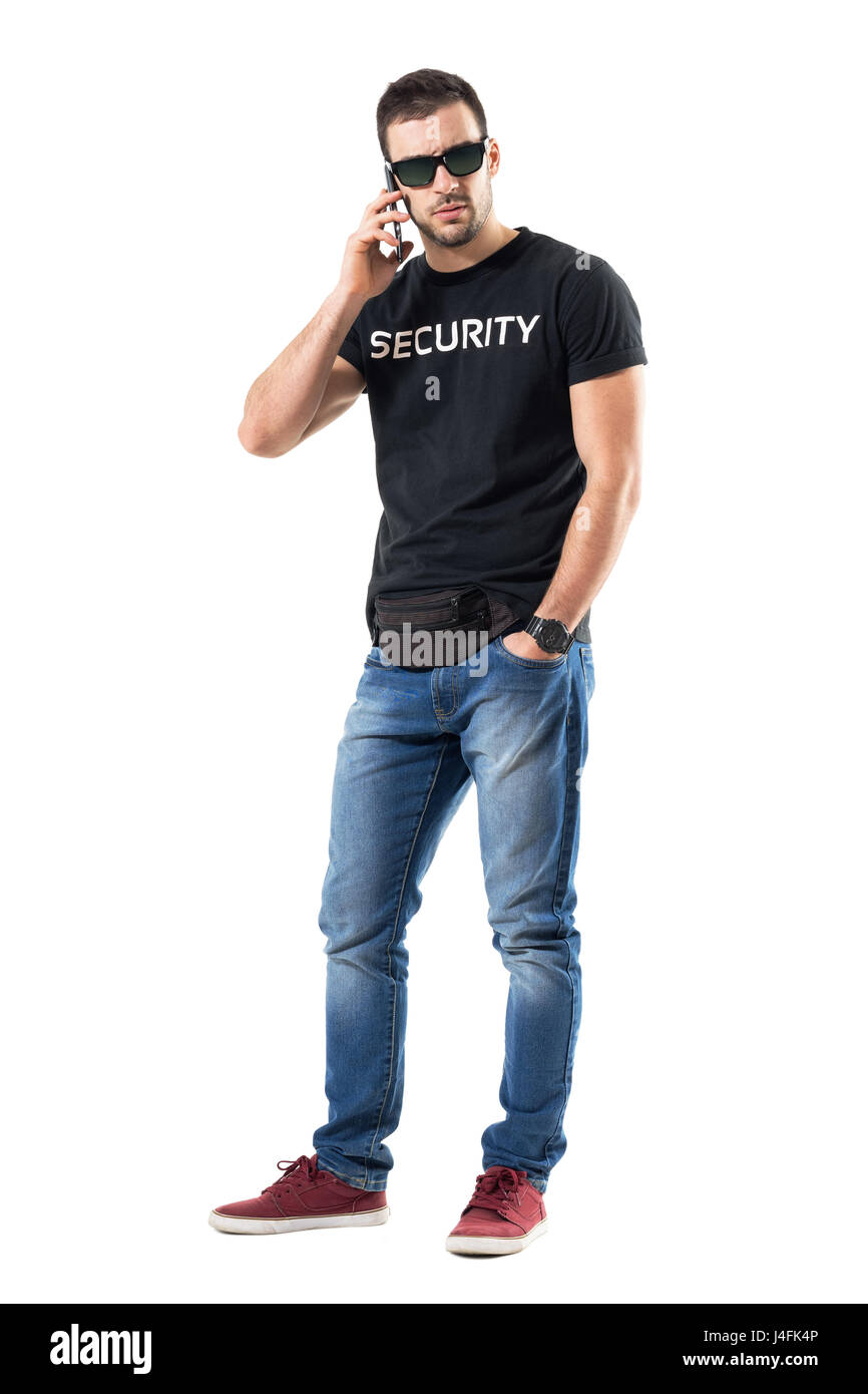 Tough serious undercover policeman talking on the phone looking at camera. Full body length portrait isolated on white studio background. Stock Photo