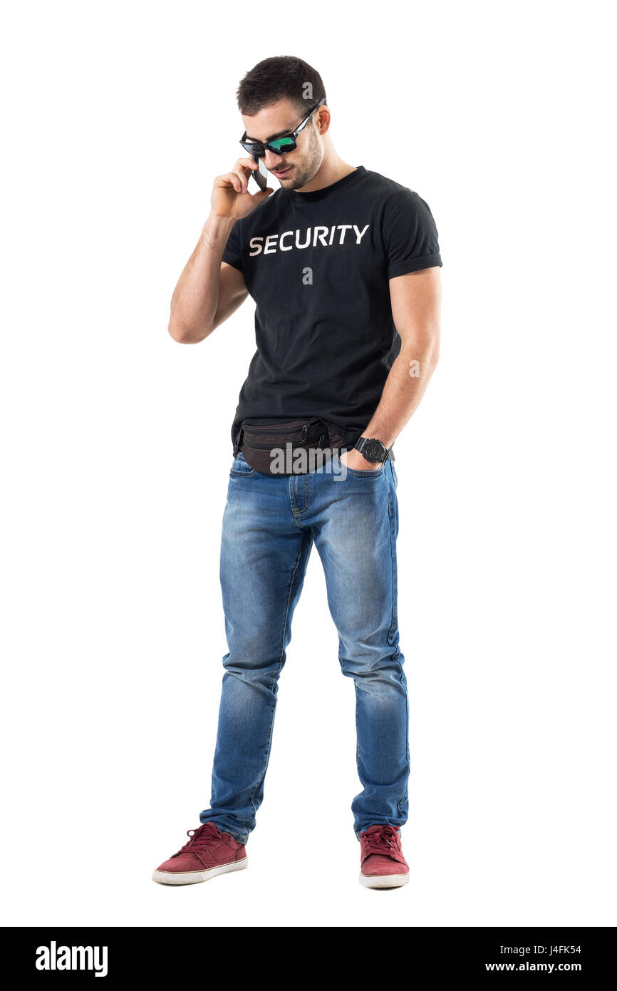 Smiling happy relaxed undercover policeman talking on the phone looking down. Full body length portrait isolated on white studio background. Stock Photo