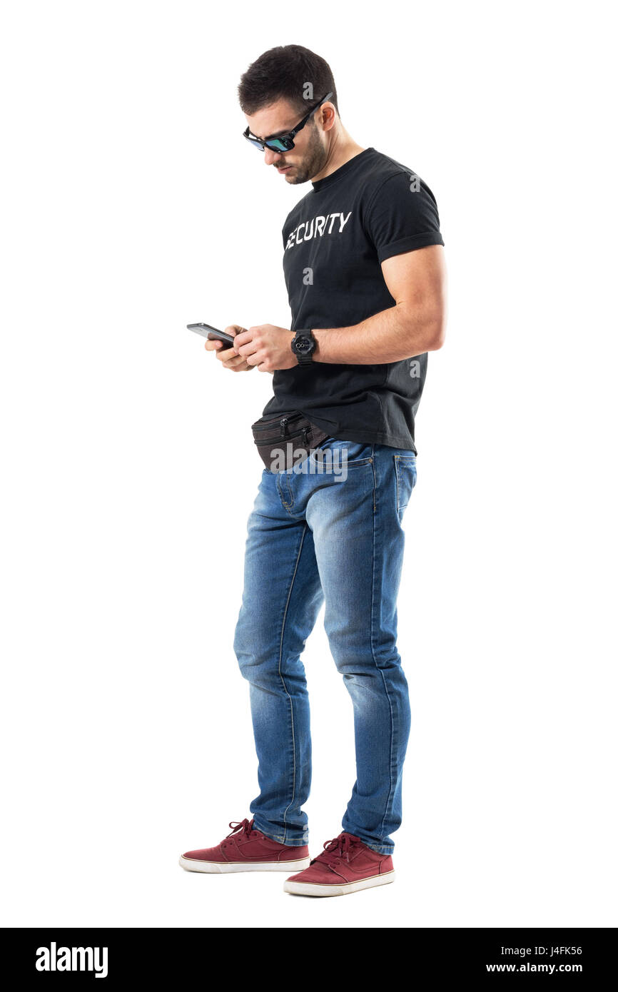 Side view of young undercover policeman typing message on mobile phone. Full body length portrait isolated on white studio background. Stock Photo
