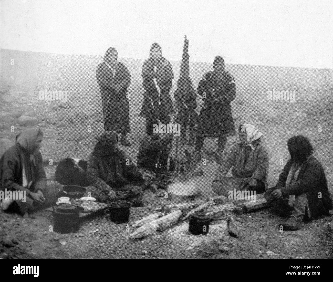 A 1914 photograph or artwork depicting a campfire gathering of the Samoyedic people, an indigenous group from Siberia. The scene captures traditional clothing, communal life, and the nomadic lifestyle in a cold environment. Stock Photo