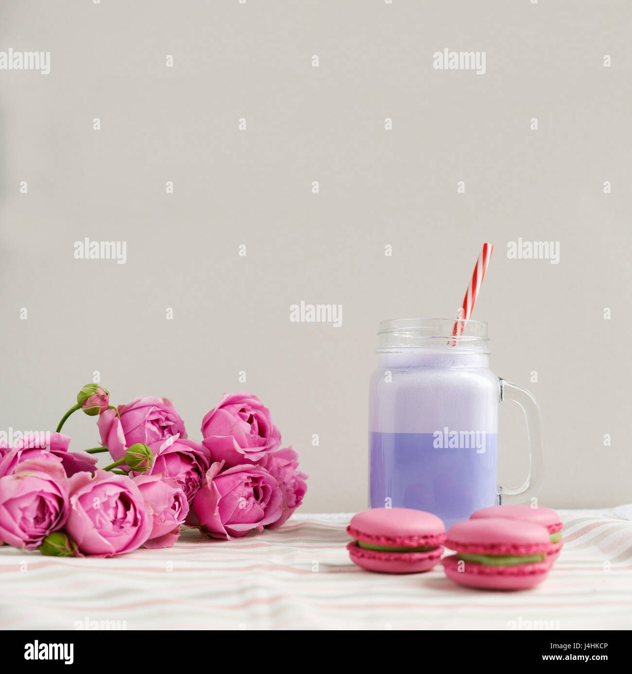 Purple coffee in stylized mason jar cup with macarons and roses and colorful decoration. Blueberry milk shake. Unicorn coffee. Unicorn food Stock Photo