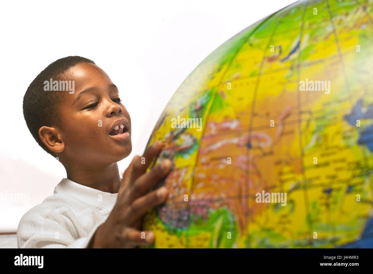 A happy healthy African American boy looking at an inflatable globe on a white background. The globe is soft focus, in the foreground and shows China Stock Photo