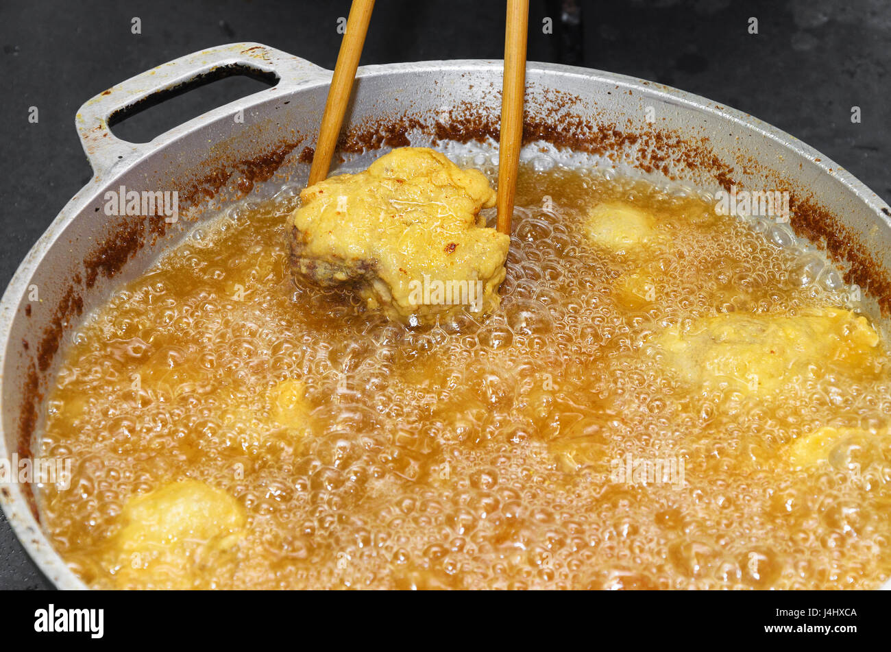 Frying fish in a pan with boiling oil. Taking out of a pan a slice of fried and breaded Pintado fish with a chopstick. Stock Photo