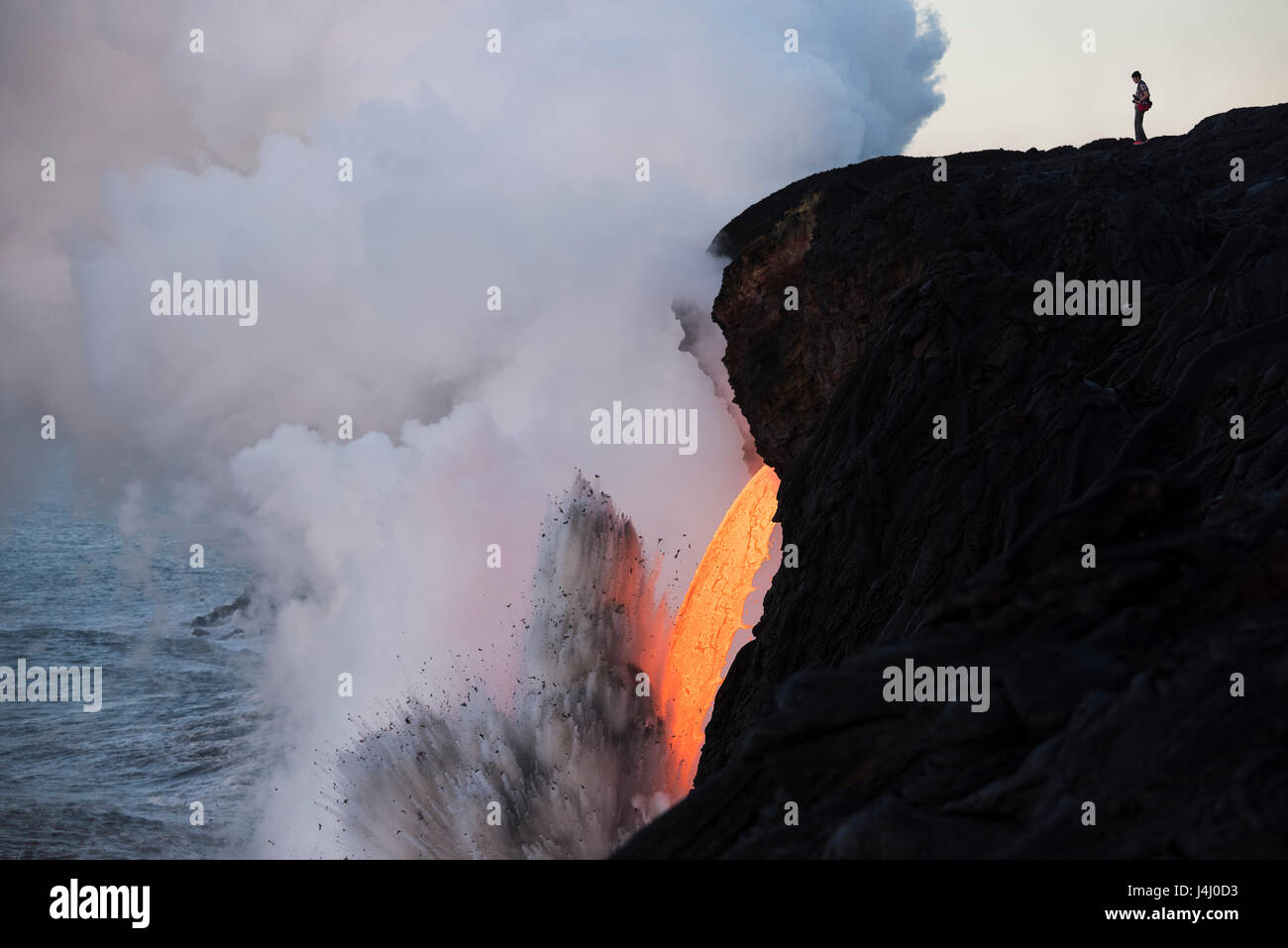 an unauthorized hiker in a restricted zone steps out onto an unstable sea cliff over a lava tube where hot lava from Kilauea Volcano enters the ocean Stock Photo