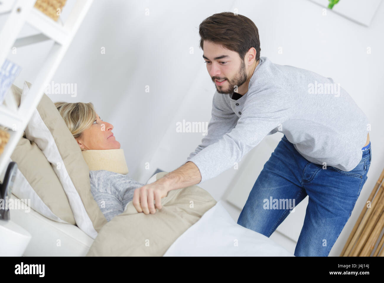 Young man pulling blanket around lady wearing neck brace Stock Photo