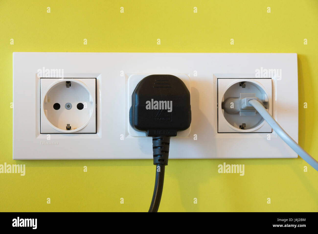 A british three-pin plug with a travel adapter plugged in next to a european two-pin plug Stock Photo