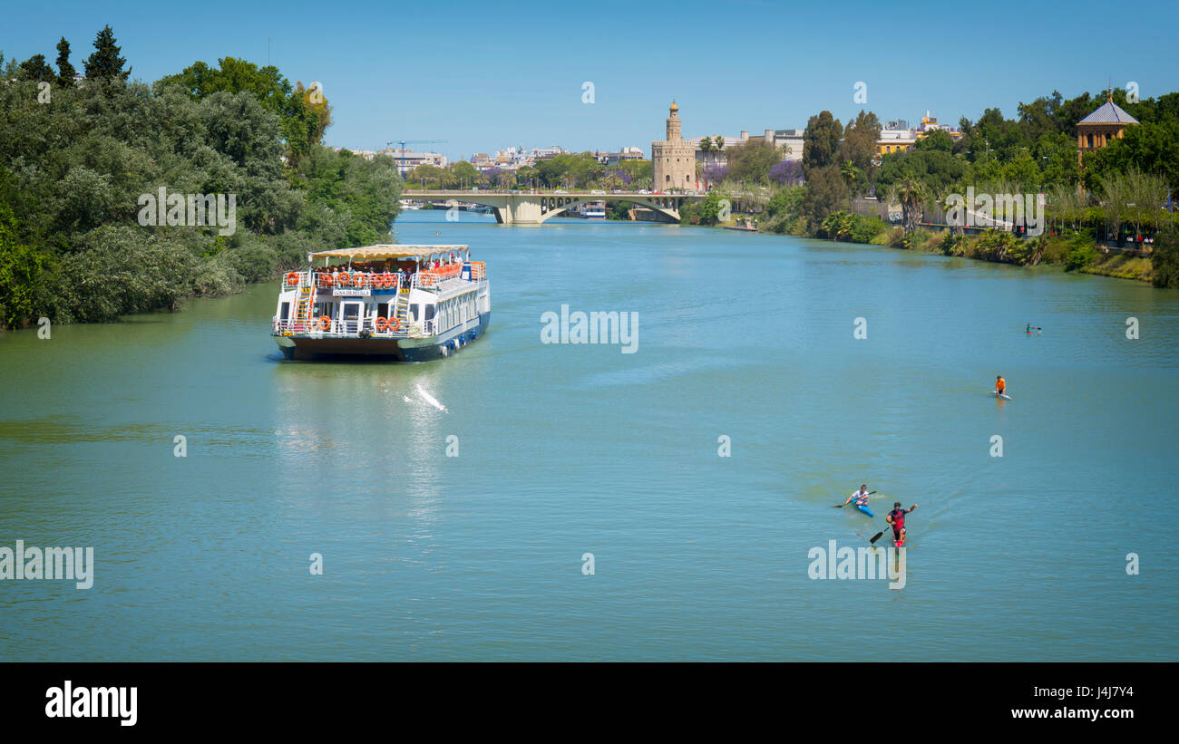 Seville, Seville Province, Andalusia, southern Spain.  Pleasure cruise boat on the Guadalquivir river. Torre del Oro (Tower of Gold) in the distance o Stock Photo
