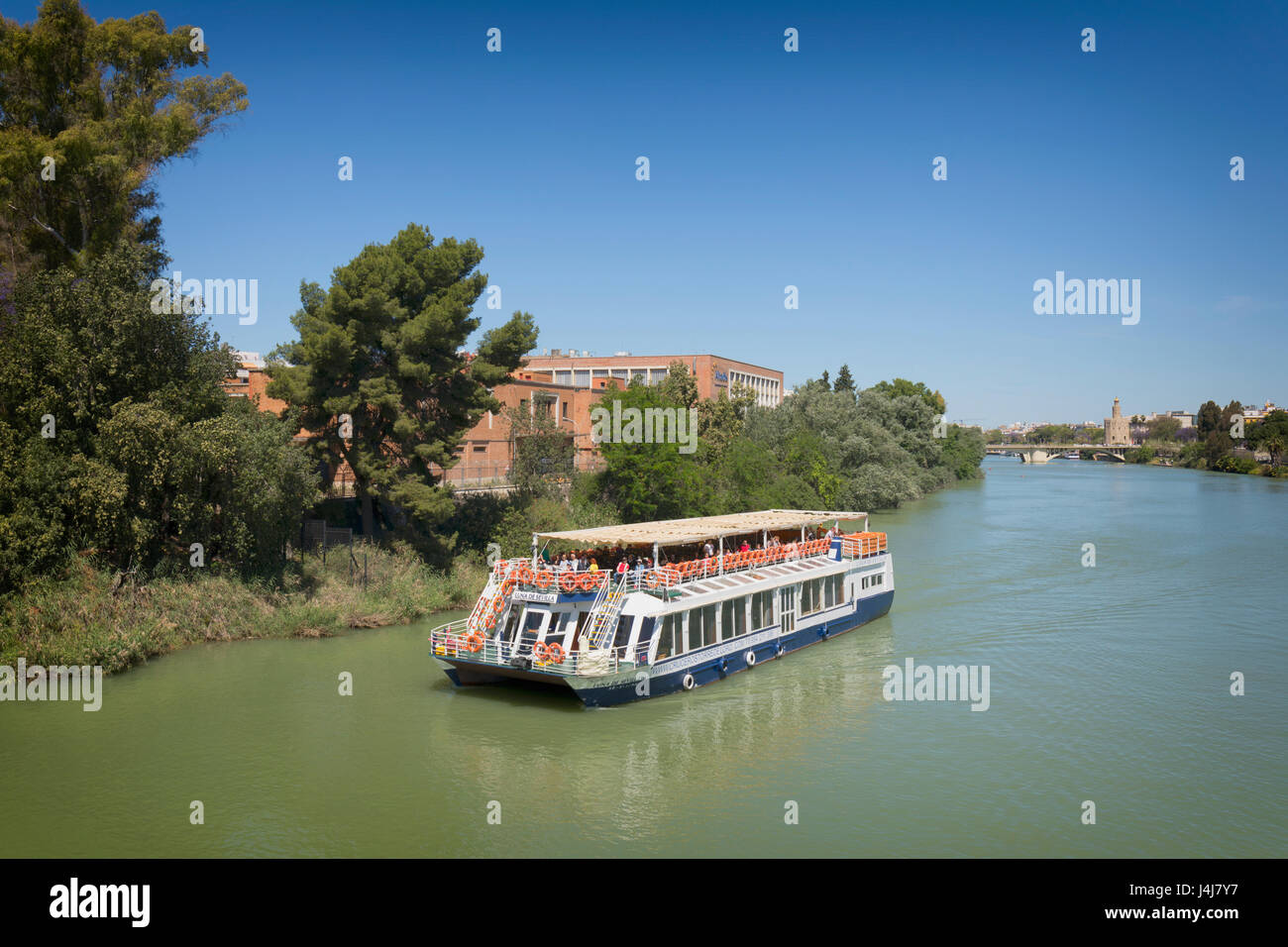Seville, Seville Province, Andalusia, southern Spain.  Pleasure cruise boat on the Guadalquivir river. Torre del Oro (Tower of Gold) in the distance o Stock Photo