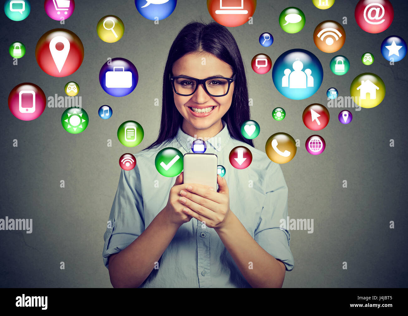 Mobile communication technology concept. Happy young woman in glasses using texting on smartphone with application symbols icons flying out of screen Stock Photo