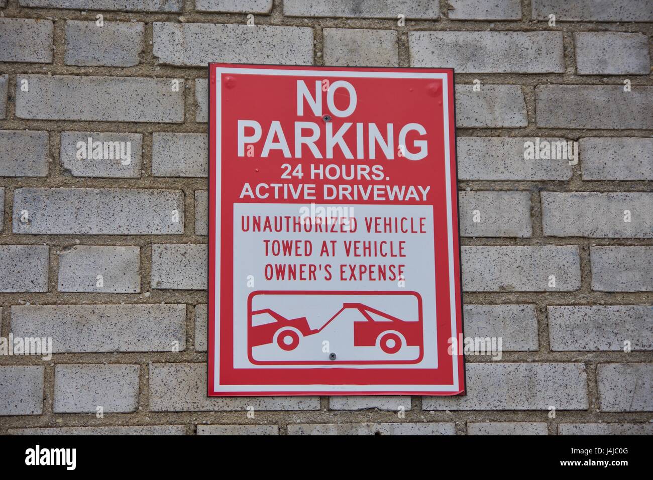 no parking sign tow at expense of owner hanging outside parking garage Stock Photo