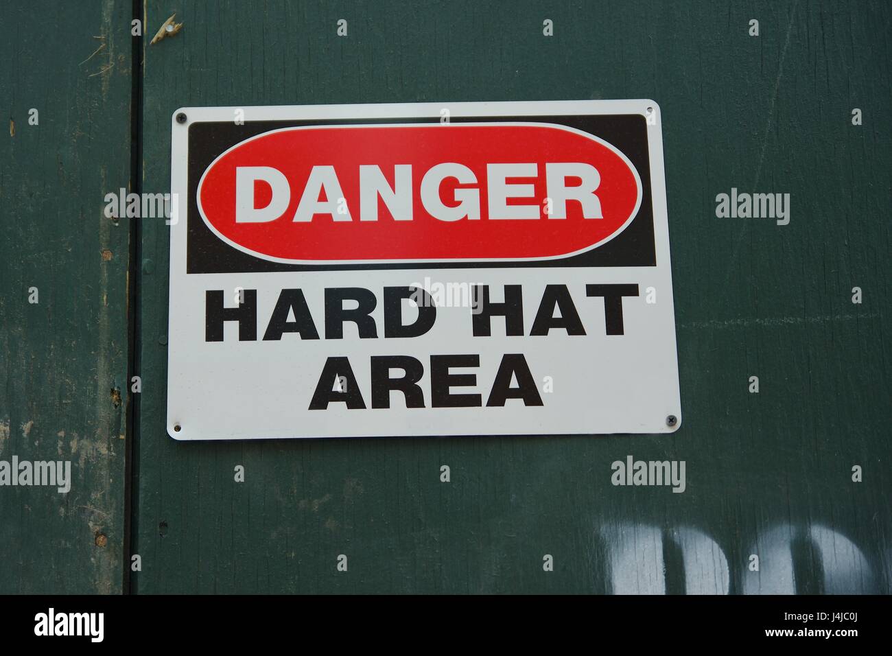 danger hard hat area sign hanging on construction green wall in urban city Stock Photo