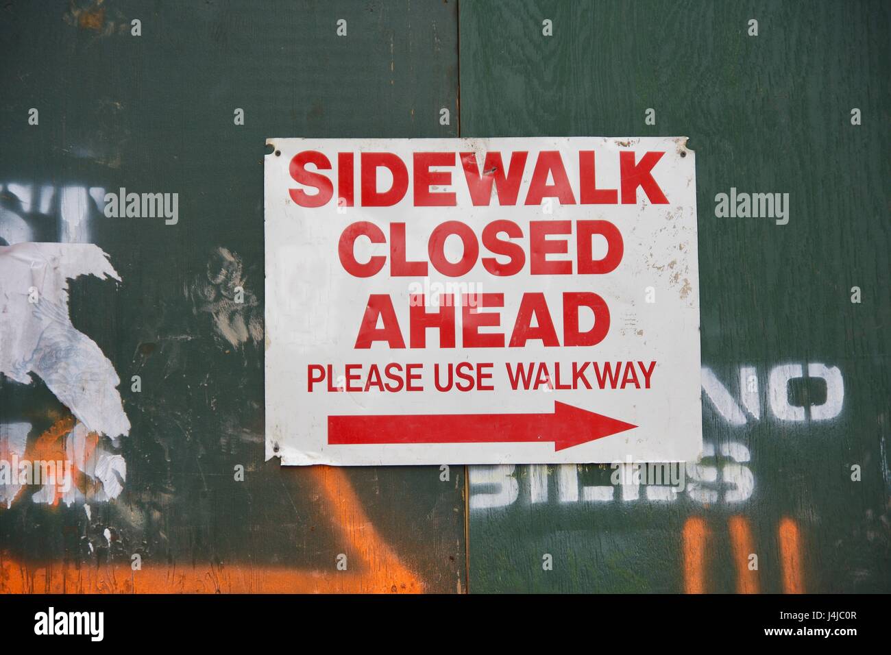 sidewalk closed ahead sign hanging on construction green wall in urban city Stock Photo