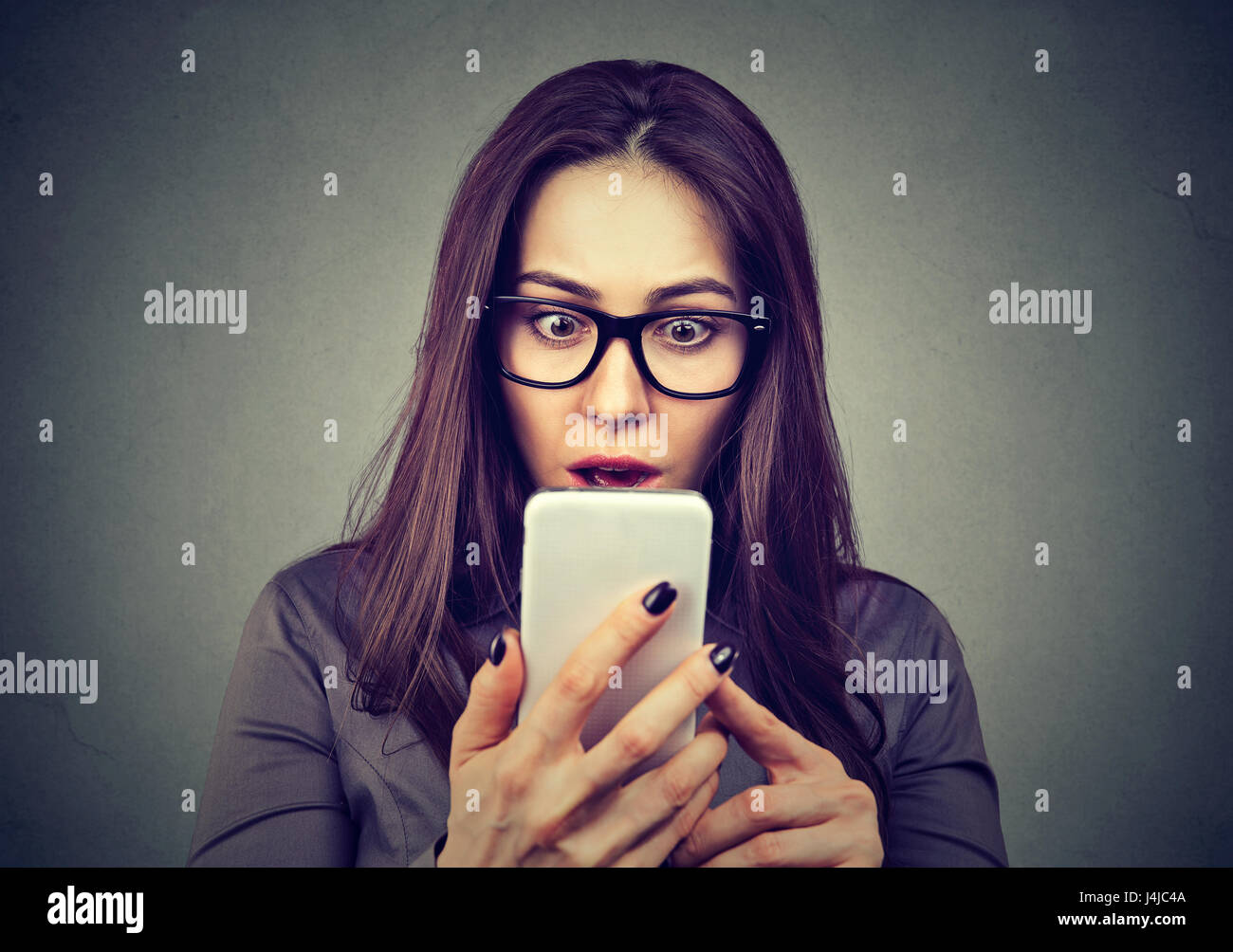 Shocked woman looking at mobile phone isolated on gray background Stock Photo