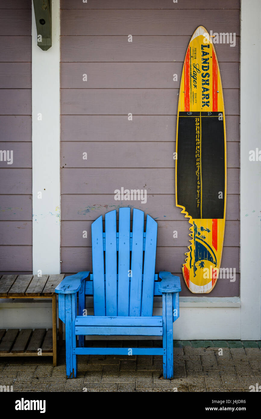 Bright blue Adirondack chair next to a surfboard with advertising for Landshark bear, in a small shopping center near Grayton beach Florida, USA. Stock Photo