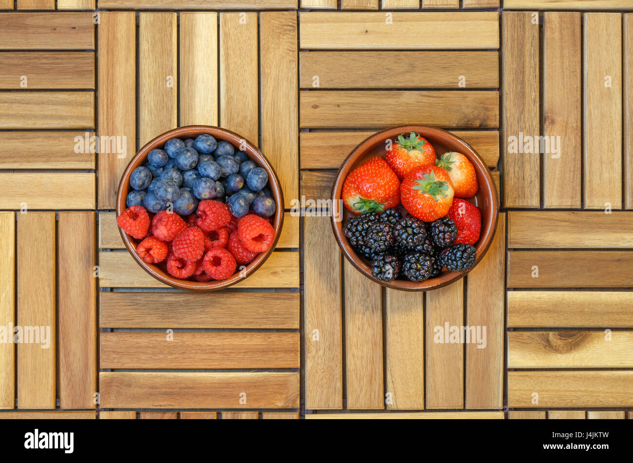 Top view of raspberries, blueberries, strawberries and blackberries in a terracotta bowl on a wooden surface Stock Photo