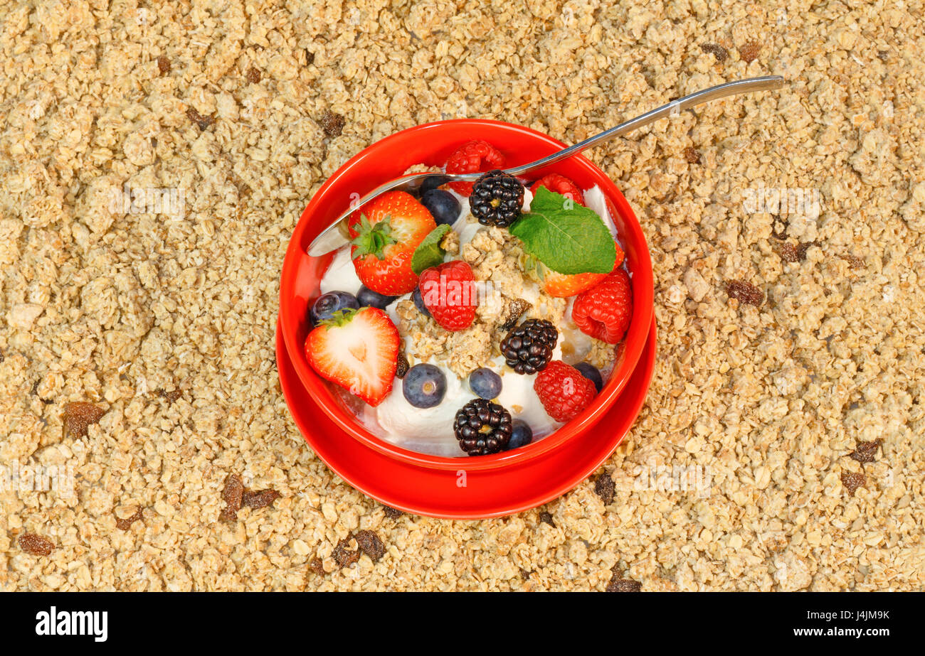 Top view of red fruit with yogurt and muesli in a red bowl against a